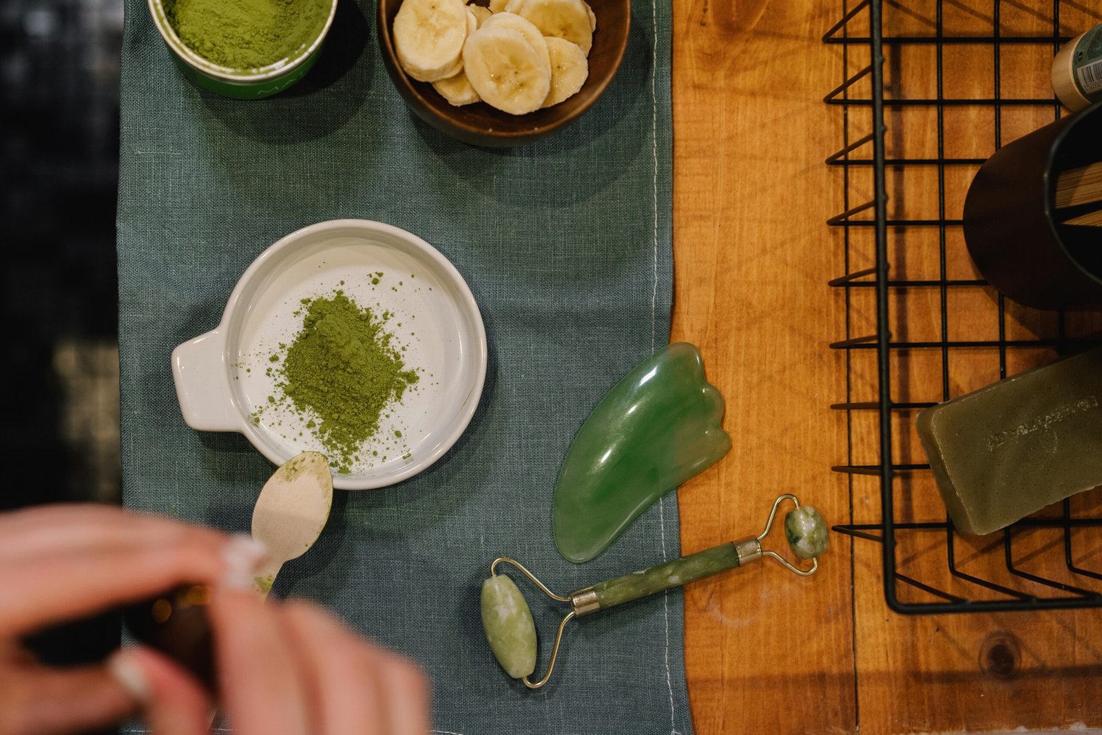 Home Flat lay of wellness products including jade roller, matcha, and banana slices on wooden table.